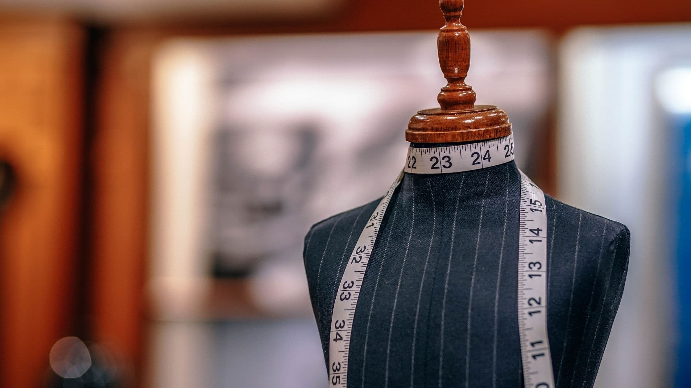 A tailor's dress form draped in pinstriped fabric with a tape measure around the neck