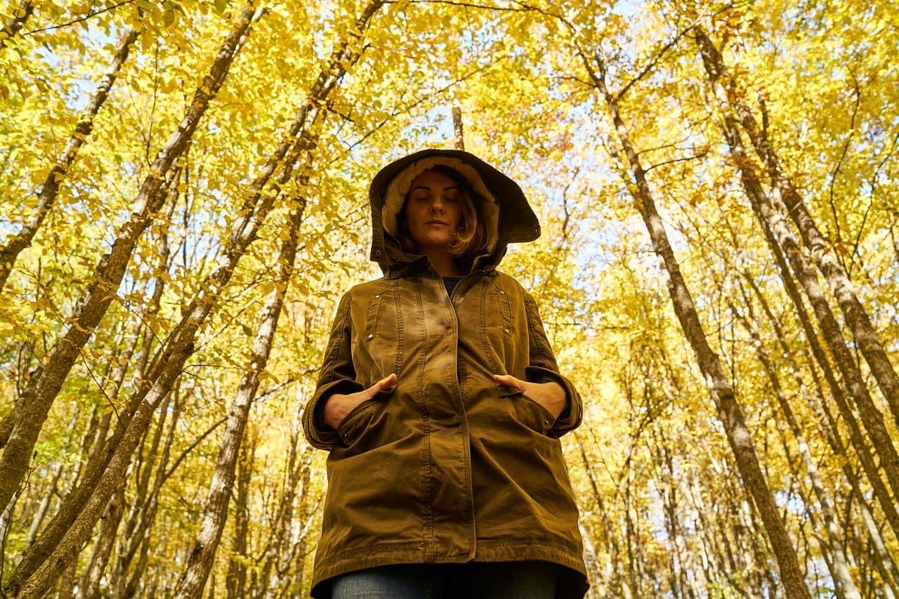 A person in a khaki jacket and wide brimmed hat standing in a yellow autumn forest