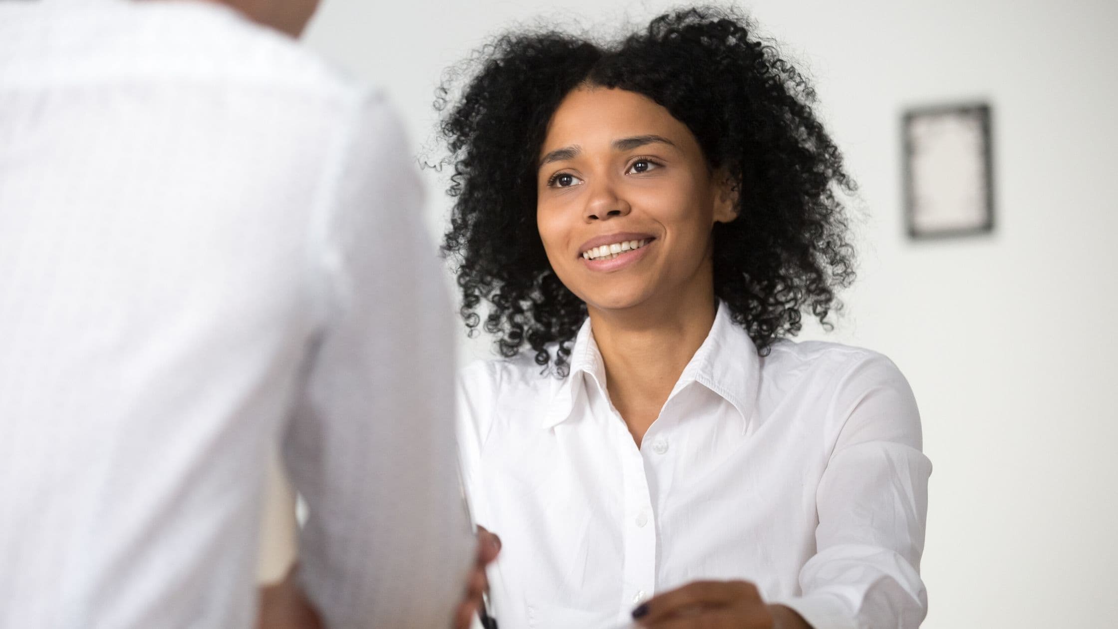 A woman in a crisp white shirt smiling as she greets someone in an office