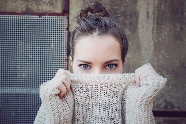 A woman pulling a chunky knit turtleneck up over the lower half of her face